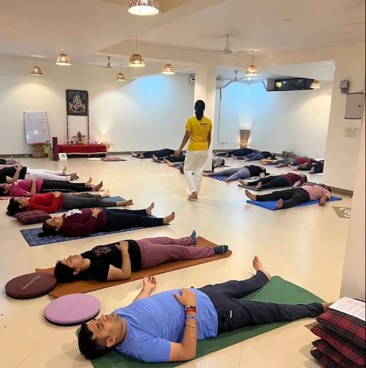 Students resting in Savasana (Final relaxation) at a Sivananda Gurgaon class, while the teacher walks between the mats.