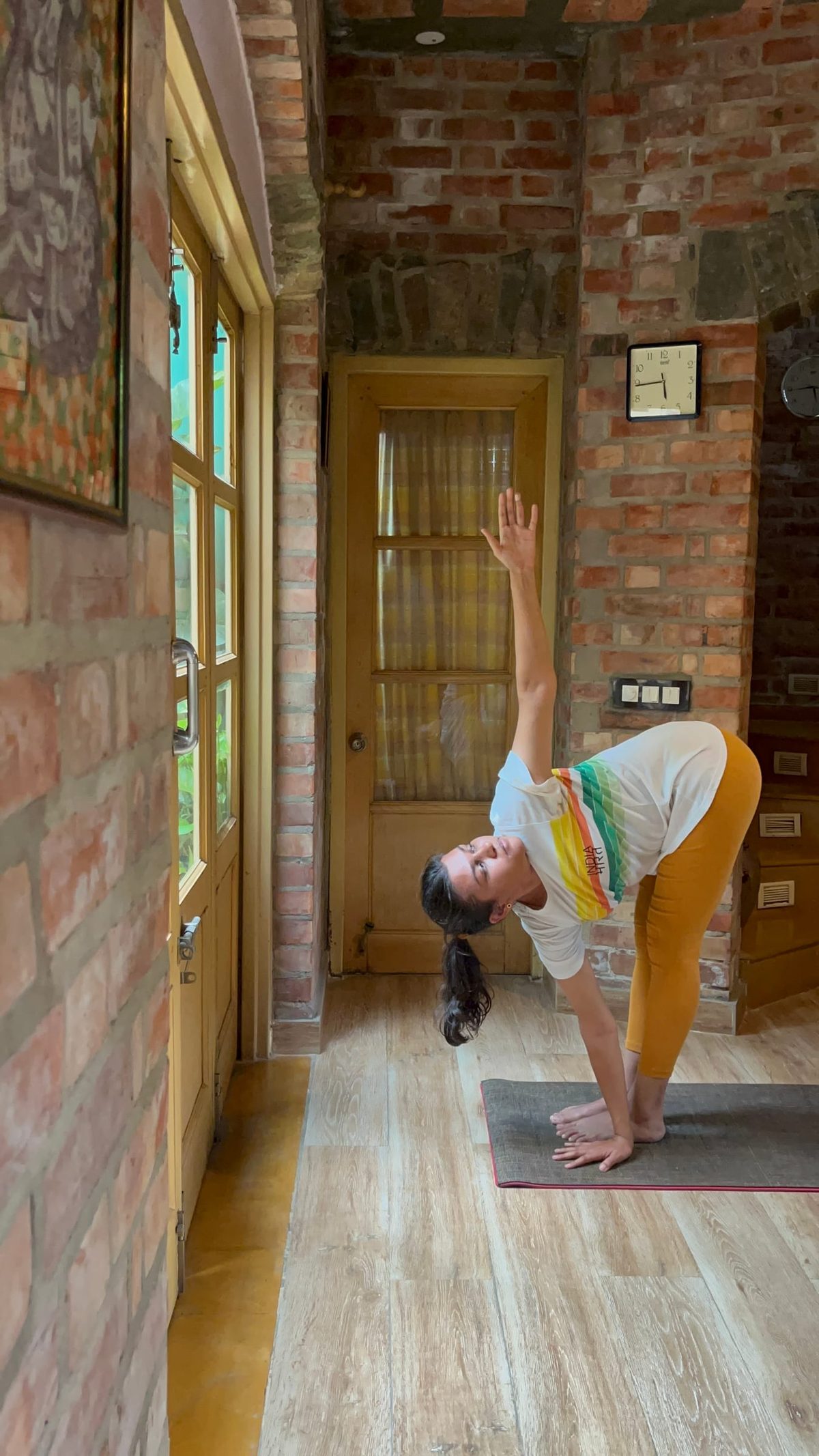 A standing forward bend revolved open, one hand to the mat and the other arm raised.