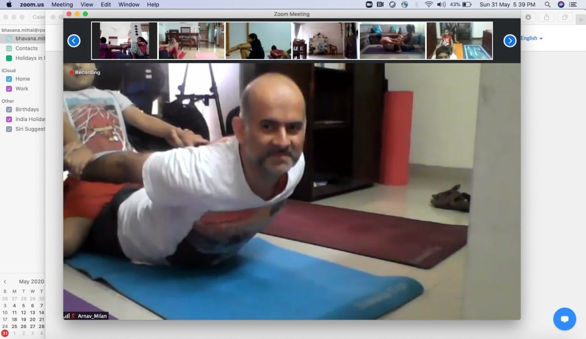 A Zoom class on a laptop — the teacher demonstrating a prone backbend in the main window, the batch in a filmstrip above.