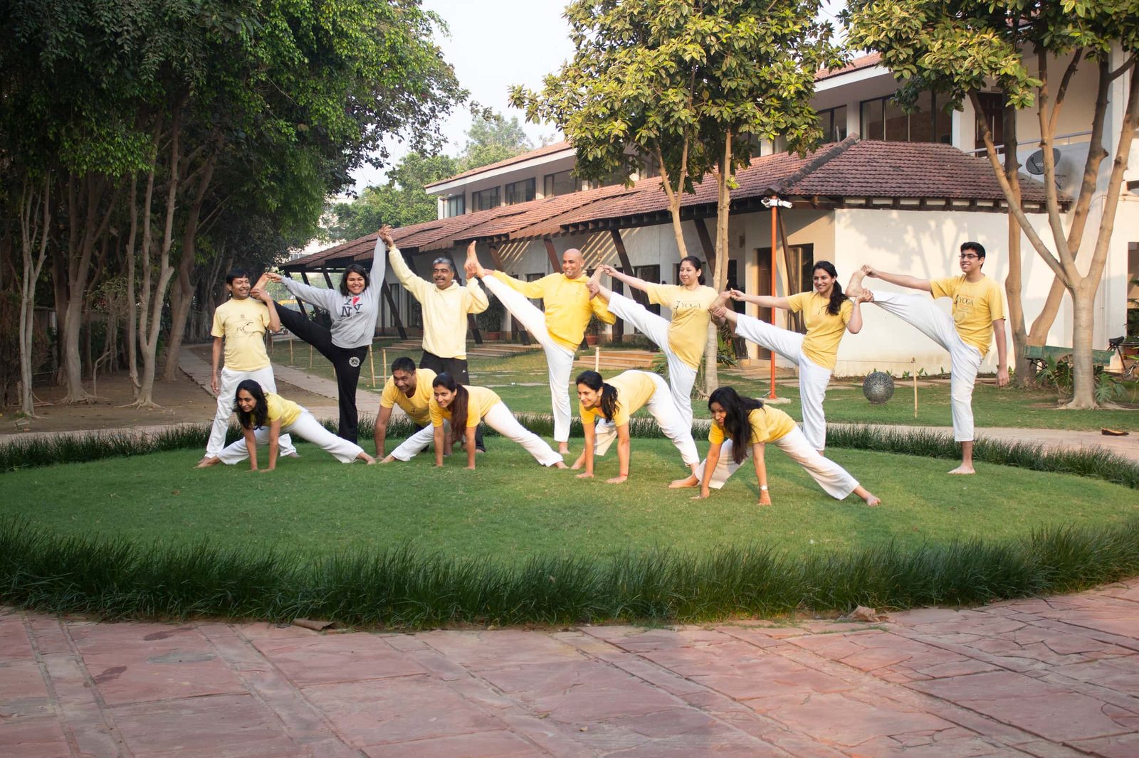 A group photographed on a lawn, most in yellow shirts, one row standing with a leg raised and one row in a wide-legged stretch