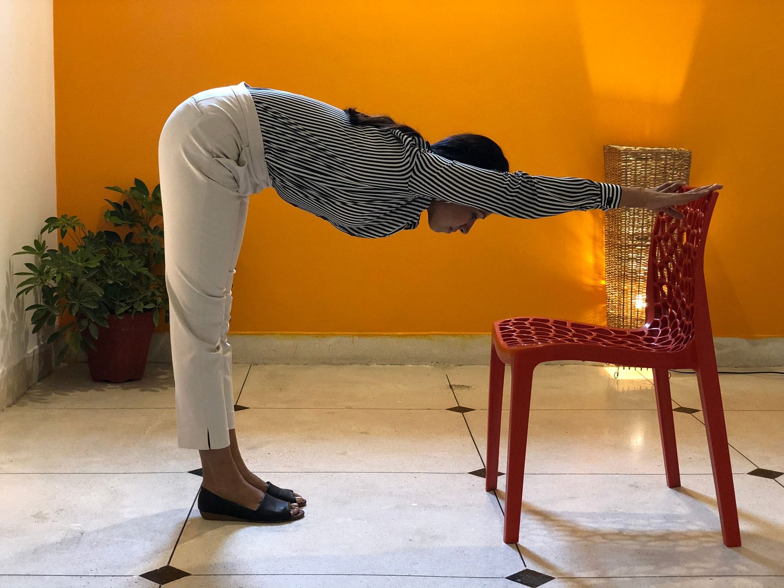 A standing forward stretch done at a chair, hands resting on the chair back