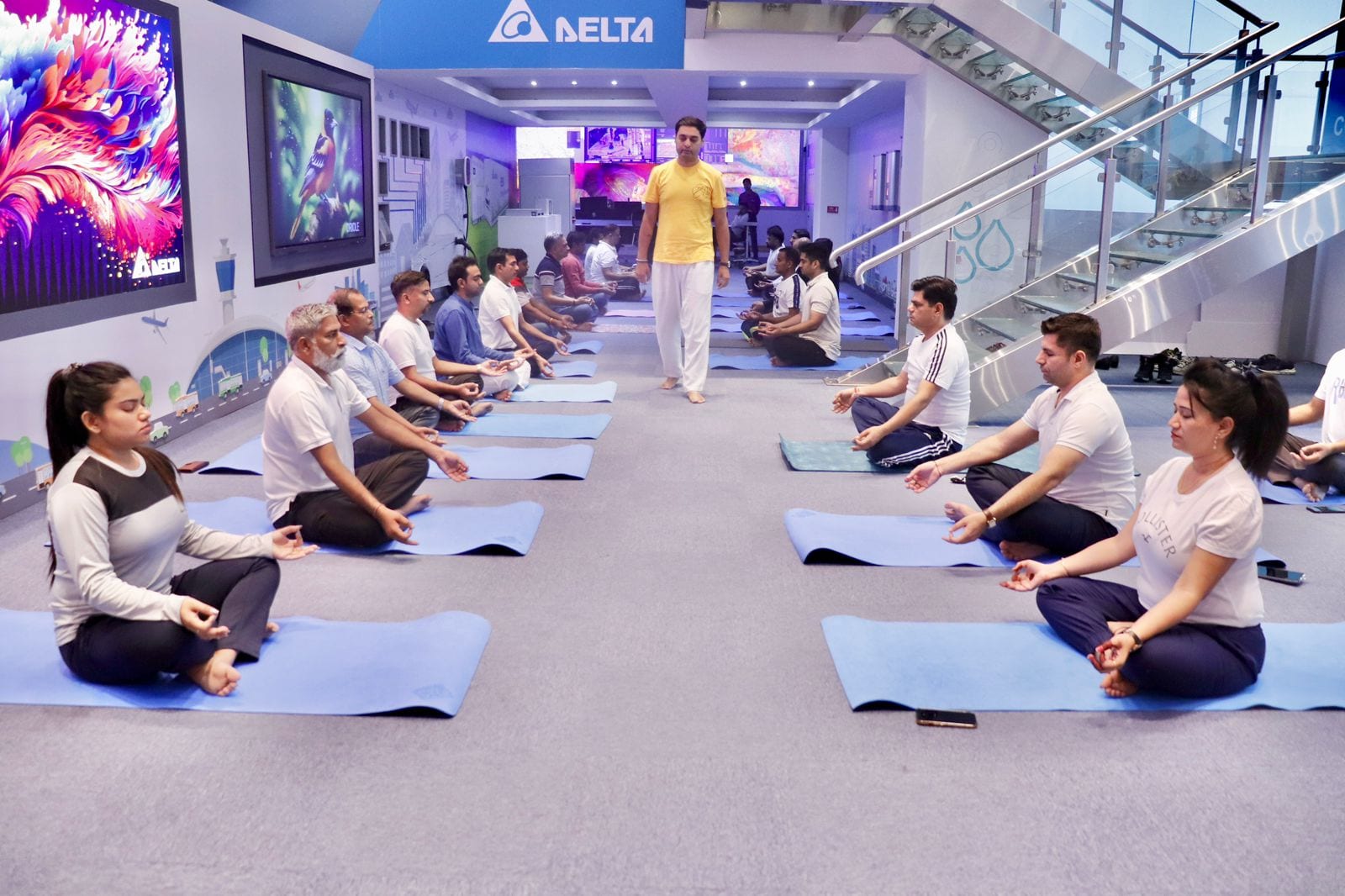 Staff seated cross-legged in meditation on mats in a showroom, the teacher walking between the rows
