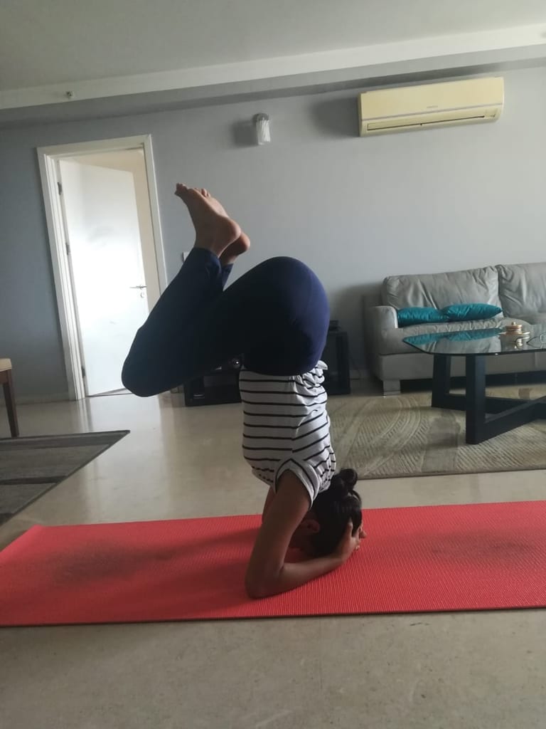 A student in Headstand on a red mat in her living room.