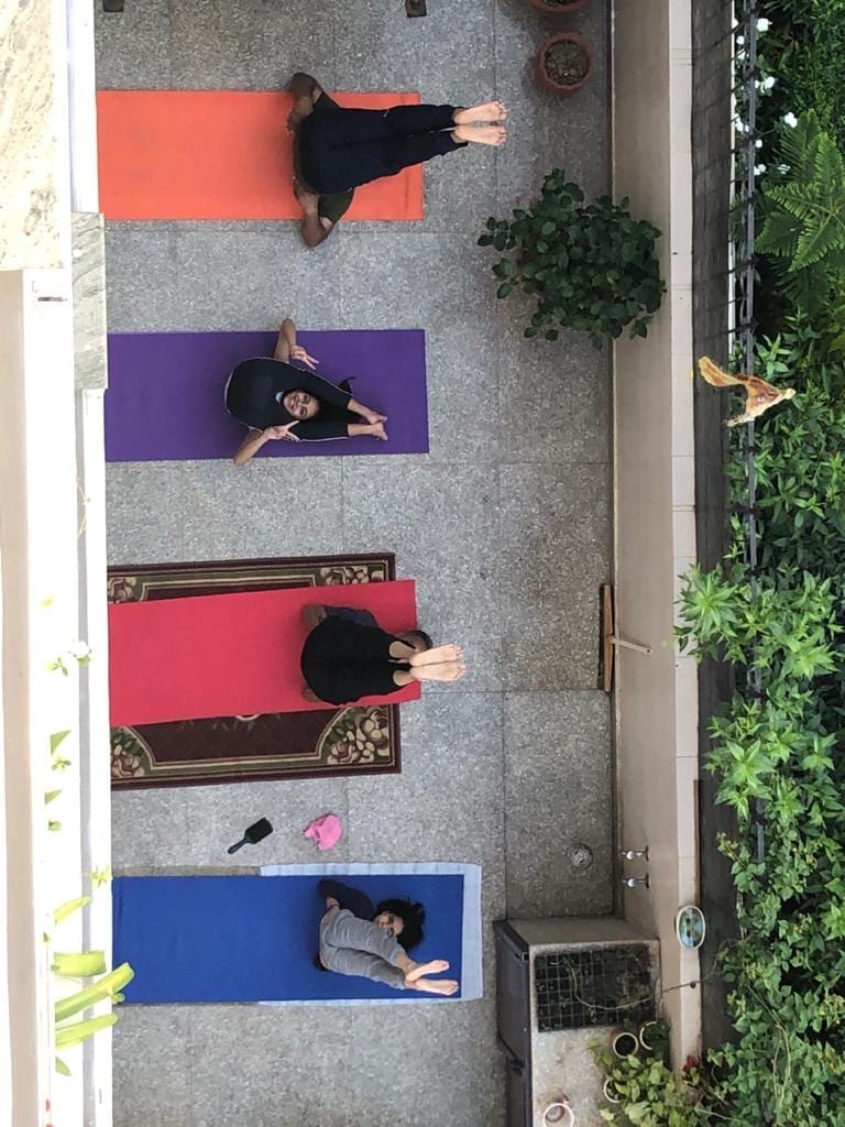 Four students in Savasana on mats along a terrace, seen from above.