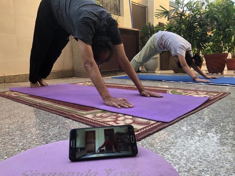 Three students in Downward Dog on mats at home, a phone on the front mat carrying the class.