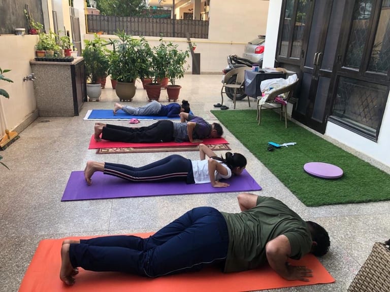 Four students in Cobra on mats along a courtyard, one behind the other.