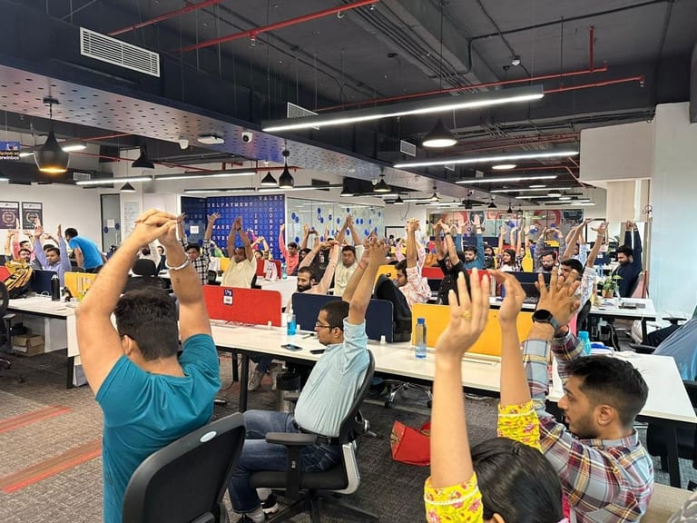 An open-plan office of staff stretching both arms overhead at their desks