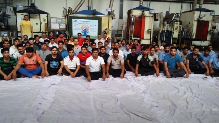 Workers seated cross-legged in rows on a factory floor