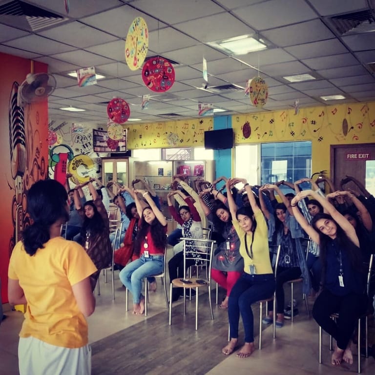 A break-room session, staff seated in a side stretch with arms overhead